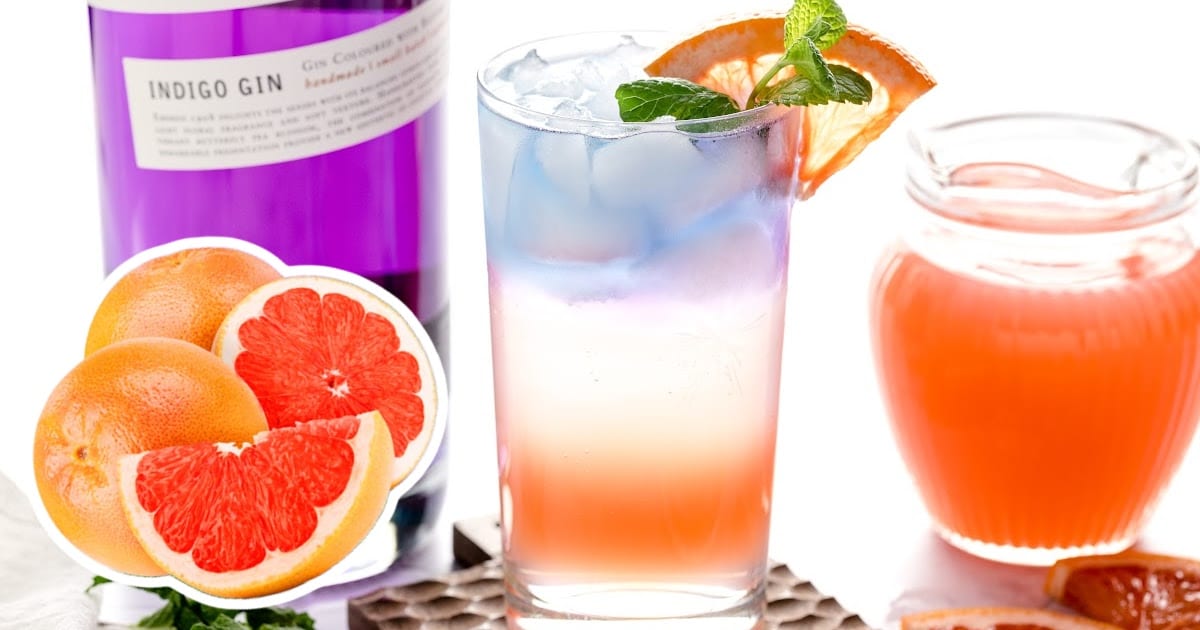 A glass of Empress Gin Cocktail with a jug of juice, two grapefruits, one cut into slices and a bottle of gin on the side