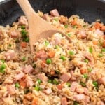 a black skillet of ham fried rice with a serving spoon in it