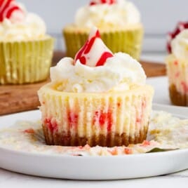 A Peppermint Cheesecake on a plate and a others on a wooden board behind it