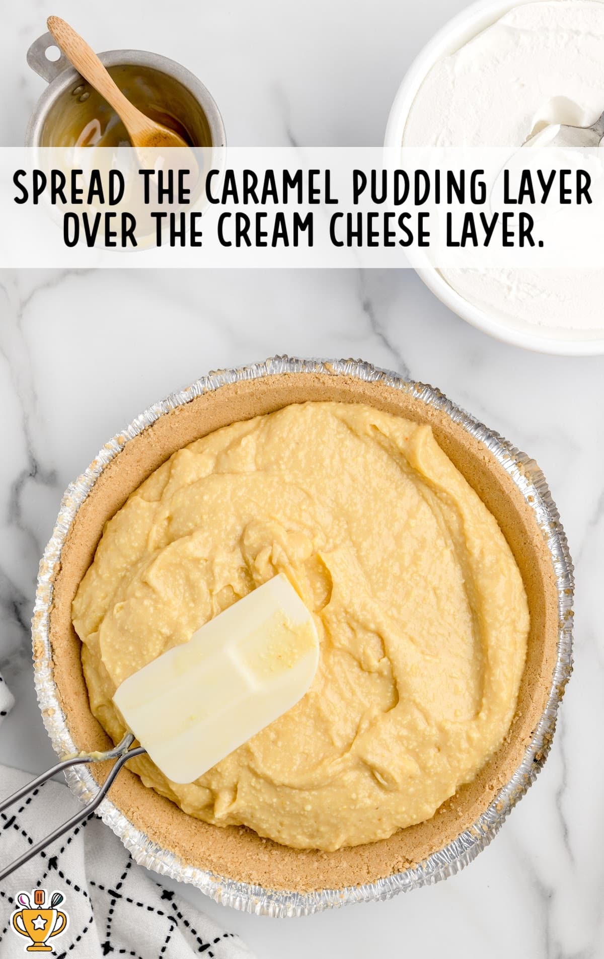 Caramel pudding spread over cream cheese layer in an aluminium foil container with a spatula in it