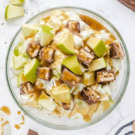 Creamy Snickers salad made with green apples, chopped Snickers bars, whipped topping, and caramel drizzle.