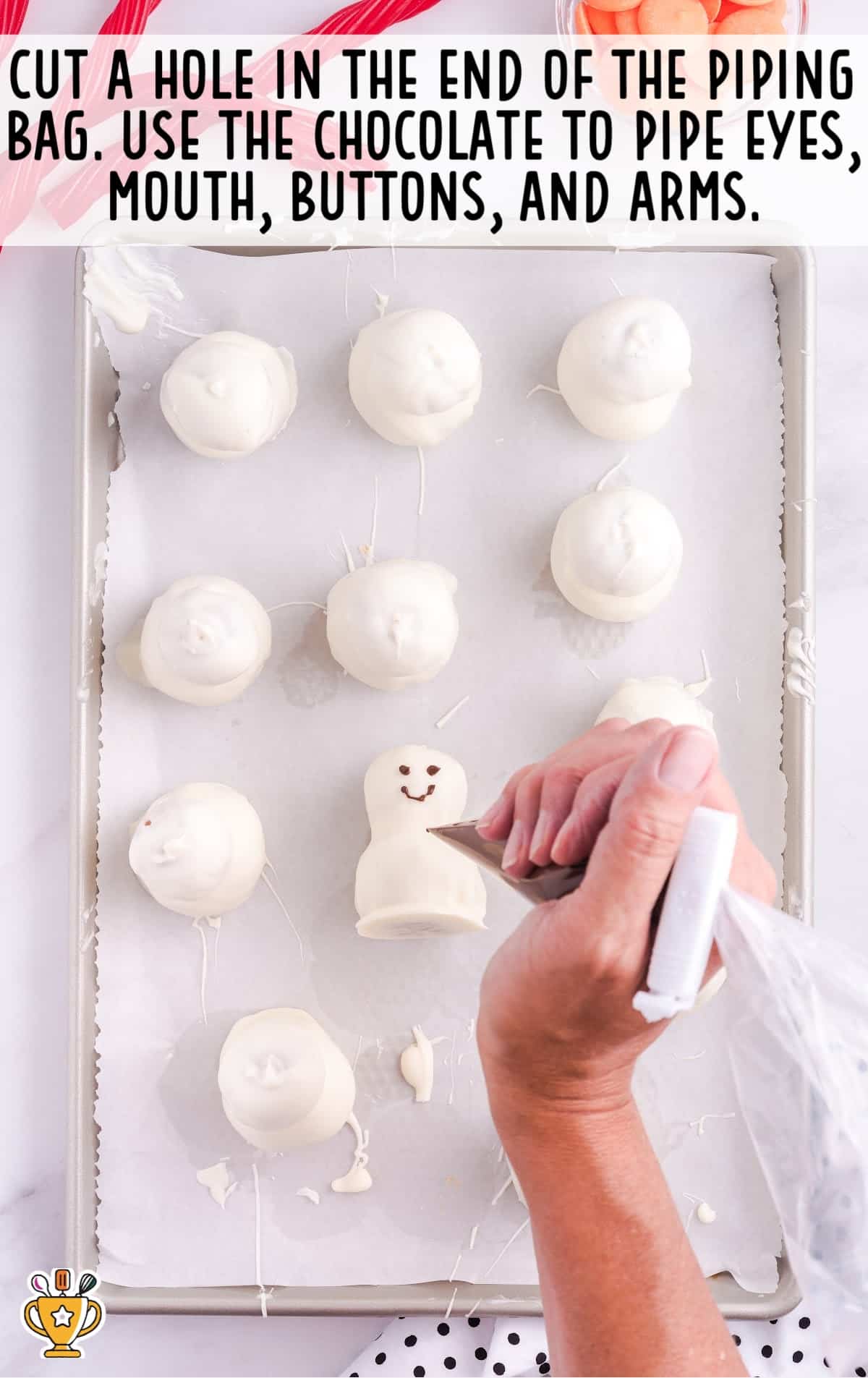 a hand piping eyes, mouth, buttons and arms on snowmen by using a piping bag