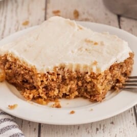 A piece of oatmeal cake with a bite missing on a white plate with a fork.