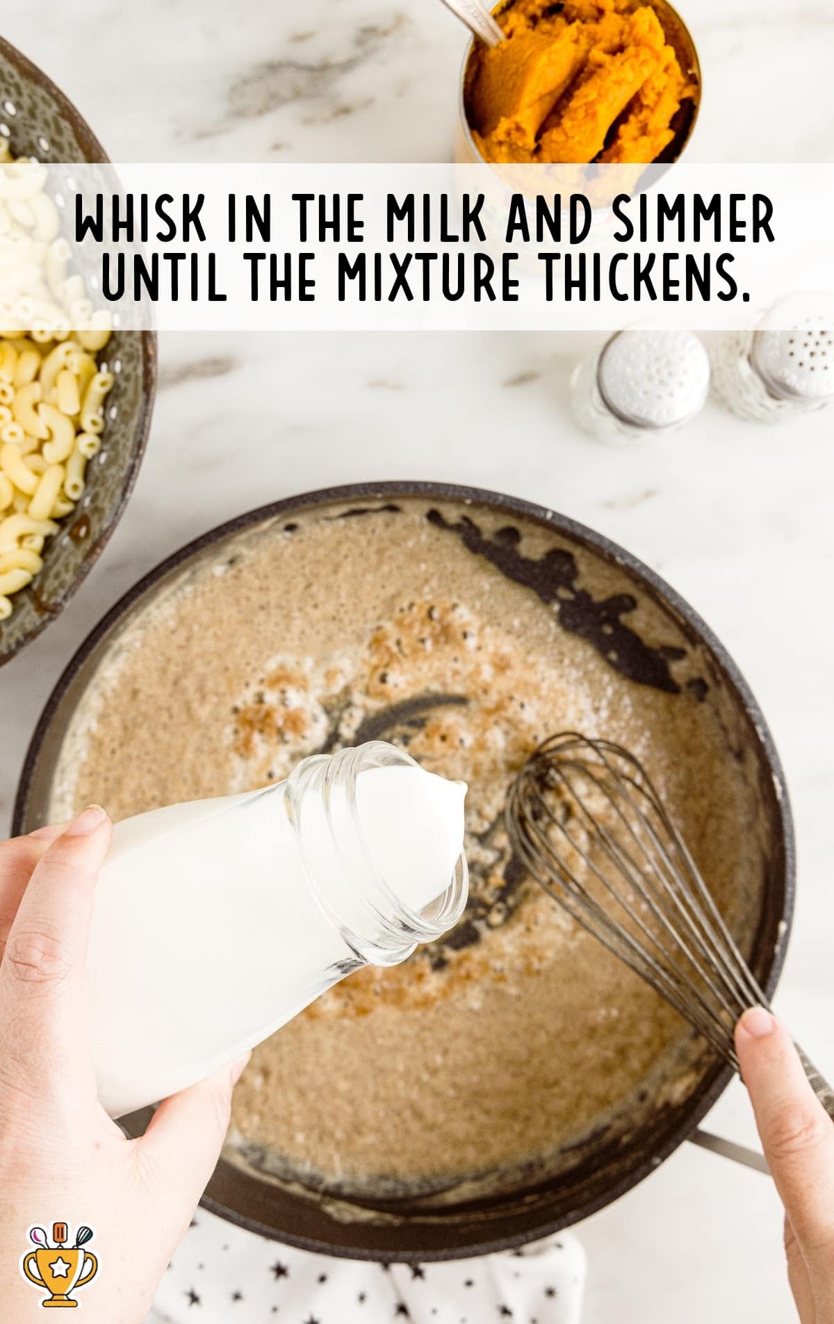 a hand pouring milk in a pan with pumpkin pie spice and a whisker on the hand