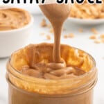 a spoon is lifting a gob of satay sauce and it's dripping down into the jar.