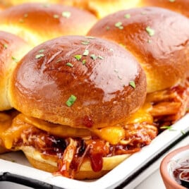 A white serving plate is covered in bbq chicken sliders.