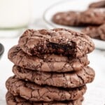A stack of brownie cookies with a bite out of the top one.