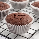 A cooling rack full of brownie muffins in white wrappers.