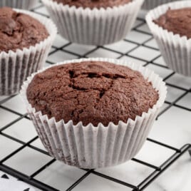 A cooling rack full of brownie muffins in white wrappers.
