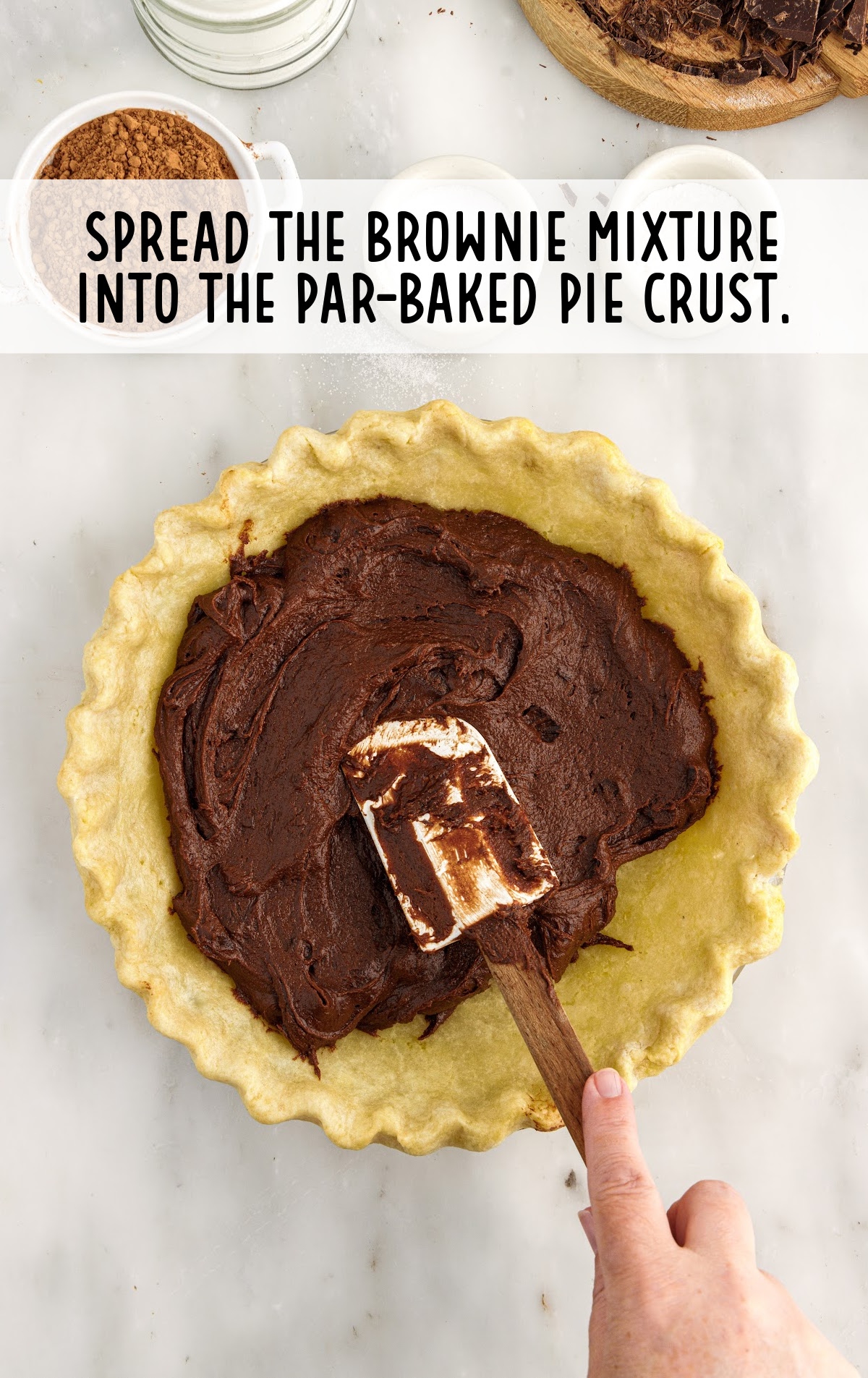 A hand with a spatula spreading brownie mixture on a pie crust