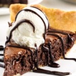 A piece of brownie pie on a white plate with ice cream and chocolate drizzle.