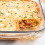 A casserole dish full of chicken taco casserole with a serving scooped out of it.