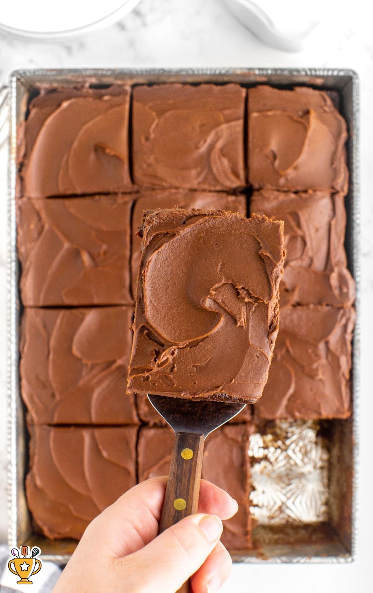 A whole cake cut into pieces, with a cake lifter removing a piece of cake.