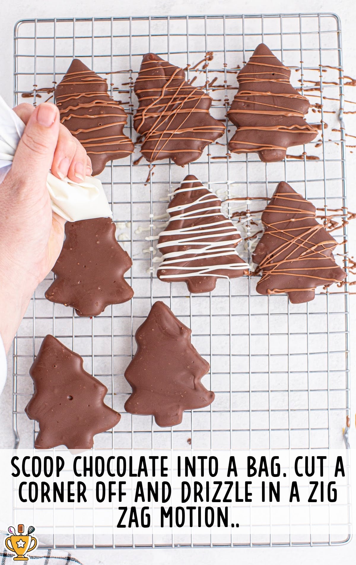 Chocolate Peanut Butter Christmas Trees on a rack with a hand drizzling some chocolate on them