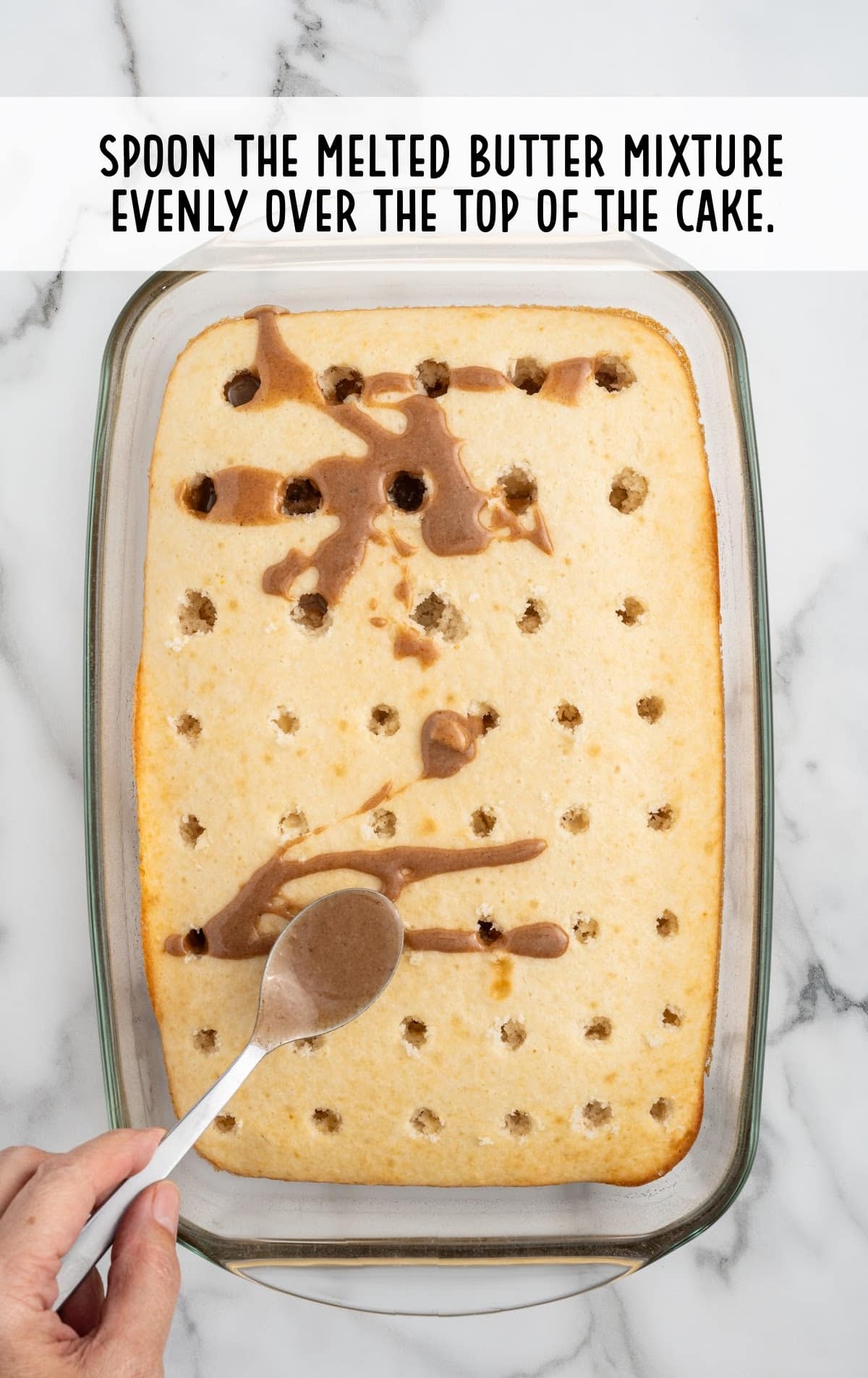 melted butter mixture spread on the cake by a hand holding a spoon