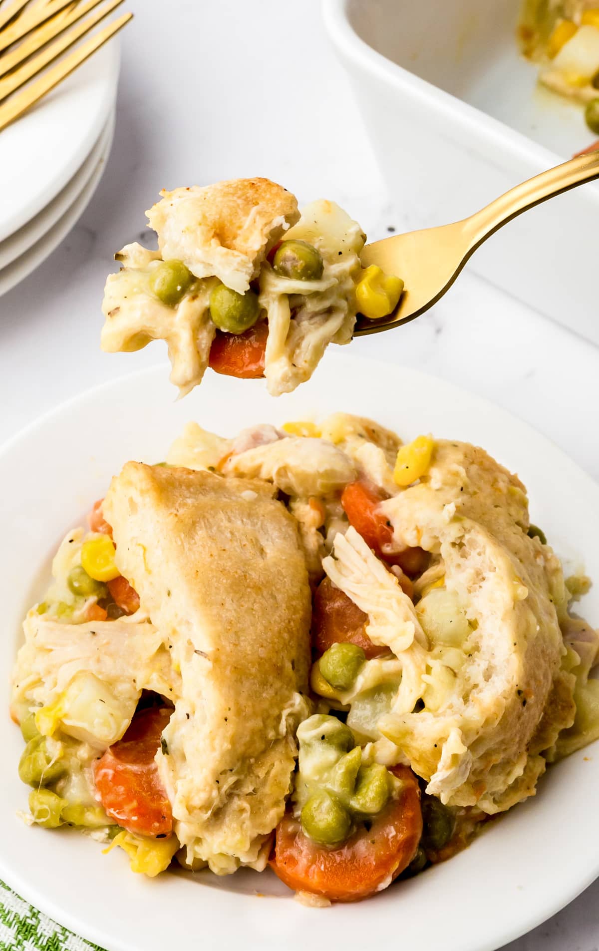 A plate of chicken pot pie holds a serving and a fork is lifting up a biteful.