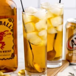 Two glasses of fireball and cream soda next to a bottle of fireball.