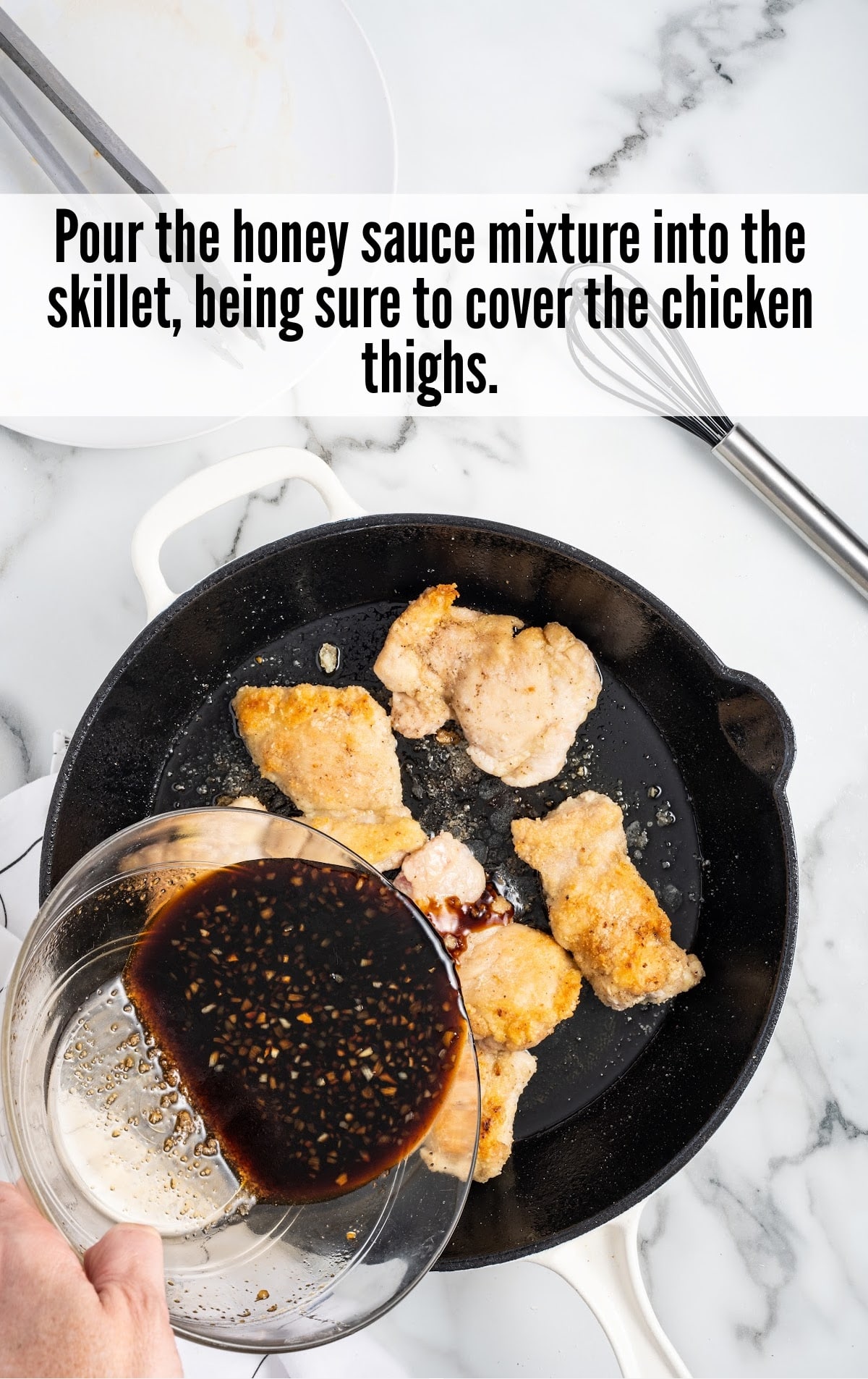 pouring honey sauce into the skillet with chicken thighs