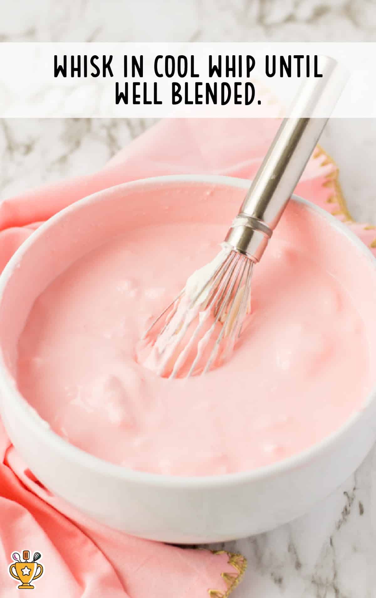 A white bowl with the cool whip whisked into the strawberry jello.