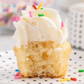 A mini cupcake on a plate with black polka dots and a big bite out of it.