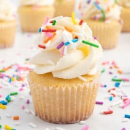 A mini cupcake with vanilla frosting and sprinkles.