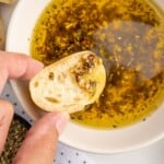 A person is dipping bread into a white bowl of Olive Oil Bread Dip.