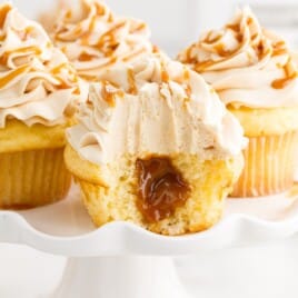 a split open Salted Caramel Cupcakes is on a white plate with other cupcakes