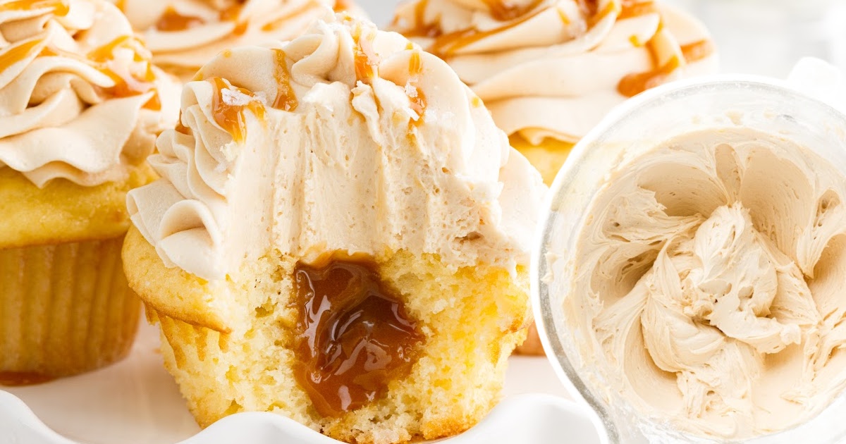 caramel is oozing from a bit open cupcake next to a bowl of frosting.