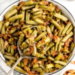 a big white bowl of Smothered Green Beans with a serving spoon in it.