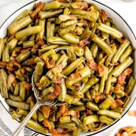 a big white bowl of Smothered Green Beans with a serving spoon in it.