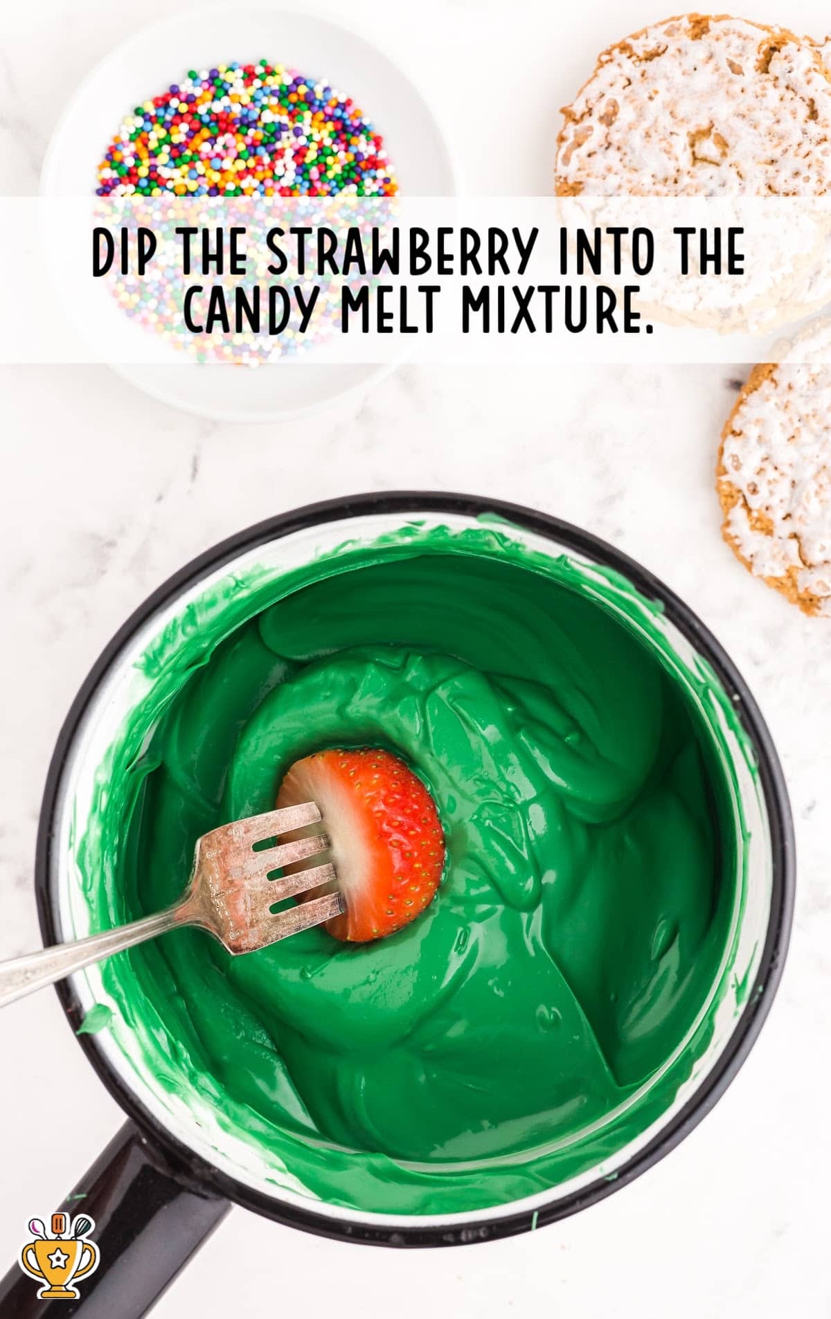 Green candy melt mixture in a pan with a fork dipping a strawberry in it