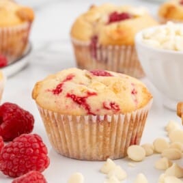 A White Chocolate and Raspberry Muffins beside raspberries and white chocolate chips.