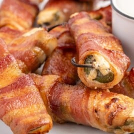 A serving plate of Bacon-Wrapped Jalapeno Poppers with a bowl of sauce for dipping.