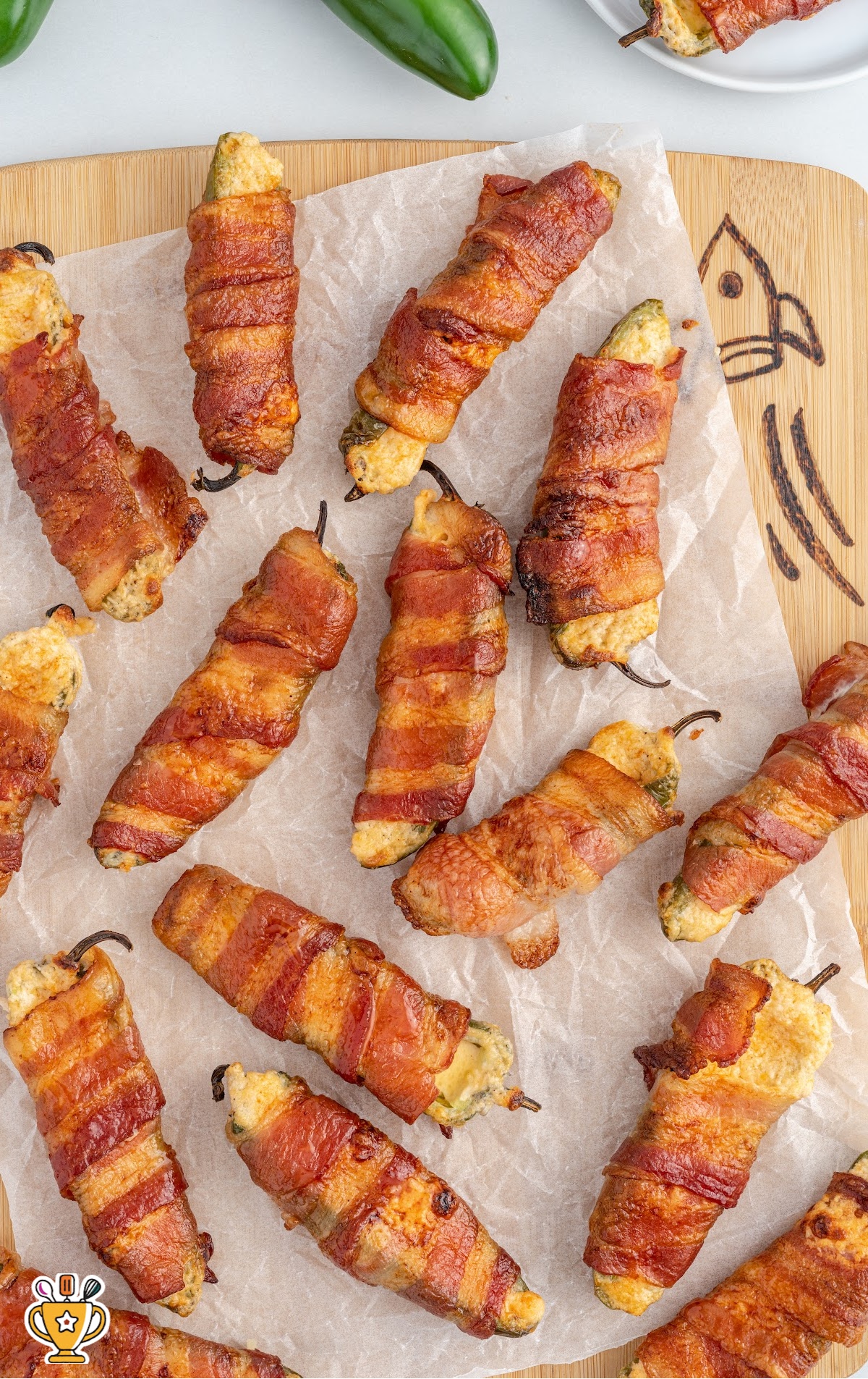 A wooden cutting board covered in parchment and Bacon-Wrapped Jalapeno Poppers.