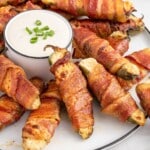 Bacon-Wrapped Jalapeno Poppers on a white serving dish with a bowl of dipping sauce.