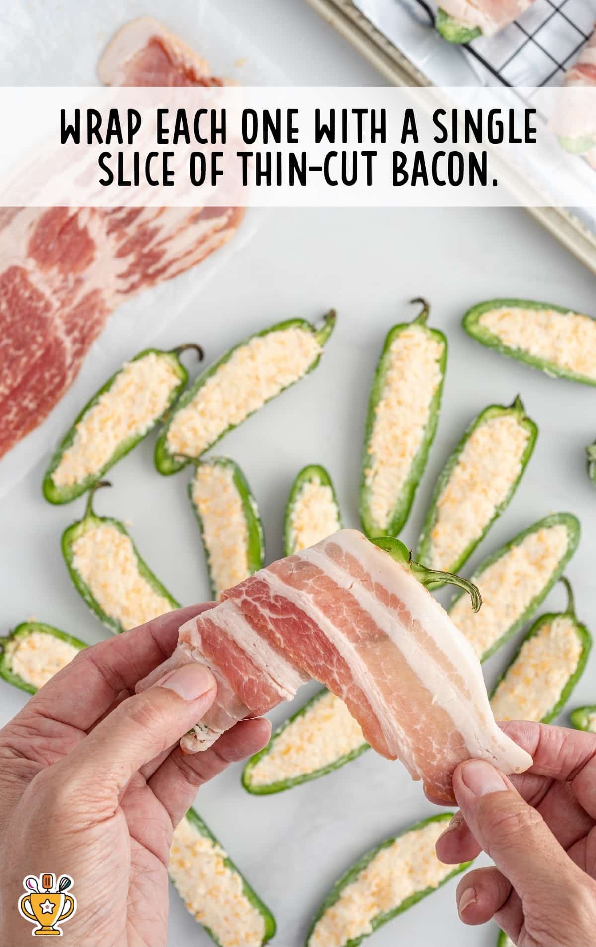 A person is wrapping slices of bacon around the stuffed peppers.