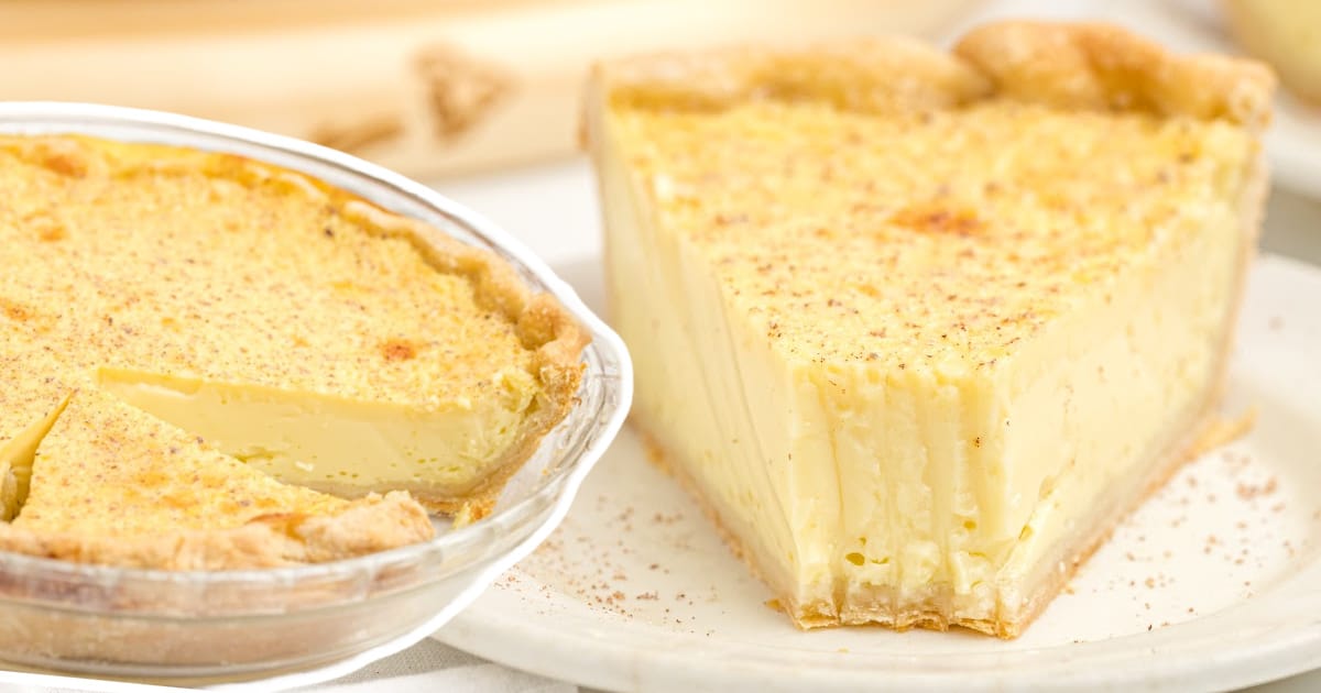 A custared pie in a glass pie plate aned a slice of pie on a white dessert plate garnished with nutmeg.