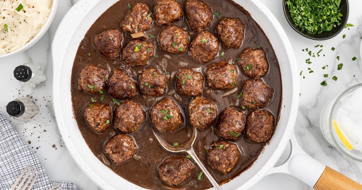 A white cooking skillet full of smothered meatballs.