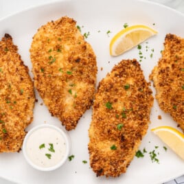 An oval plate with four pieces of panko chicken on it, garnished with lemons.