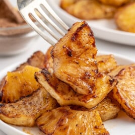 A serving of Air Fryer Pineapple on a white plate with a fork lifting up a piece.