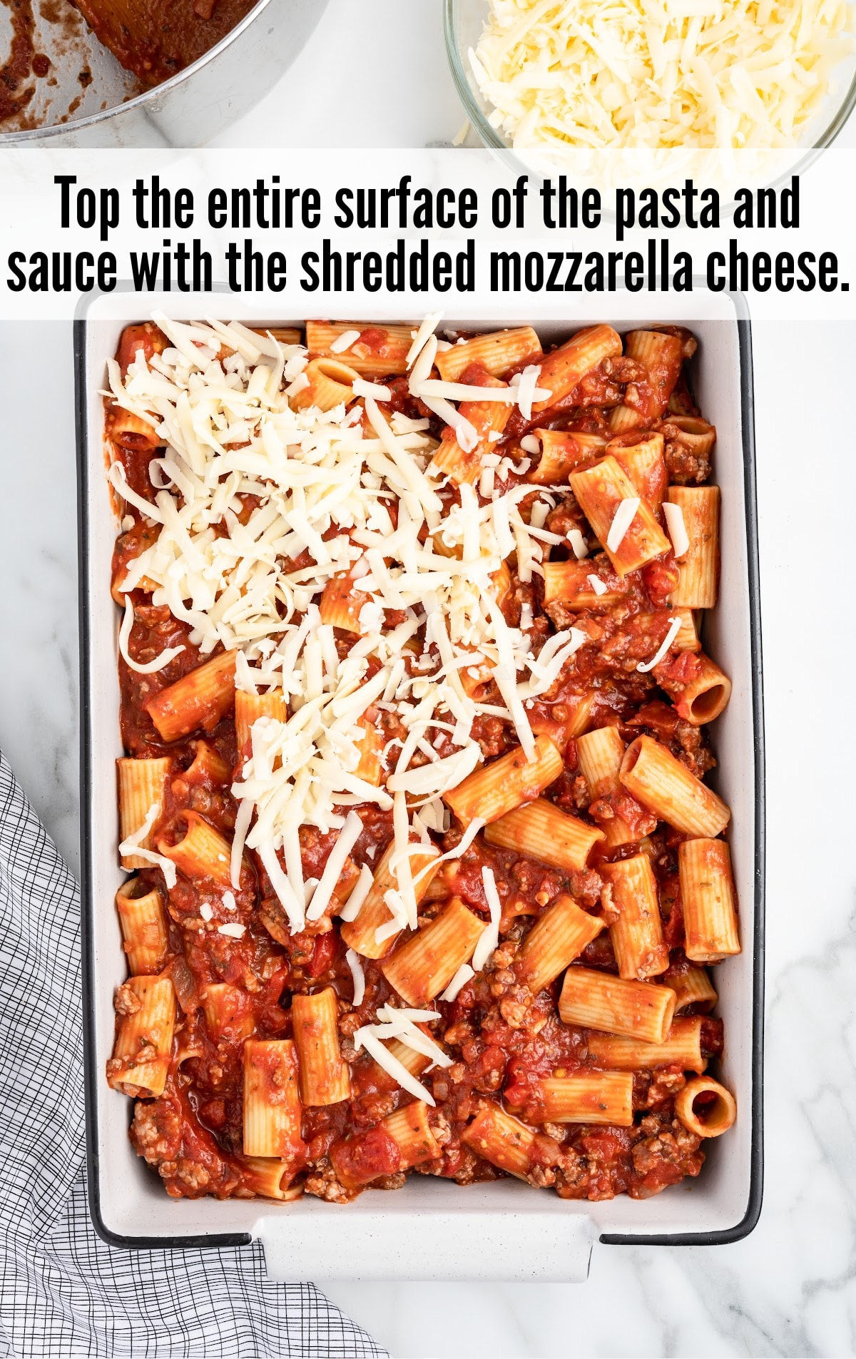 topping the surface of the pasta and sauce with the shredded mozzarella cheese
