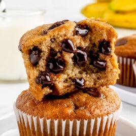 Two Banana Chocolate Chip Muffins stacked. The top one is split open to show the gooey chocolate chips.