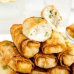 A stack of crab rangood egg rolls and the top one is cut in half to show the creamy filling.