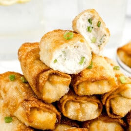 A stack of crab rangood egg rolls and the top one is cut in half to show the creamy filling.