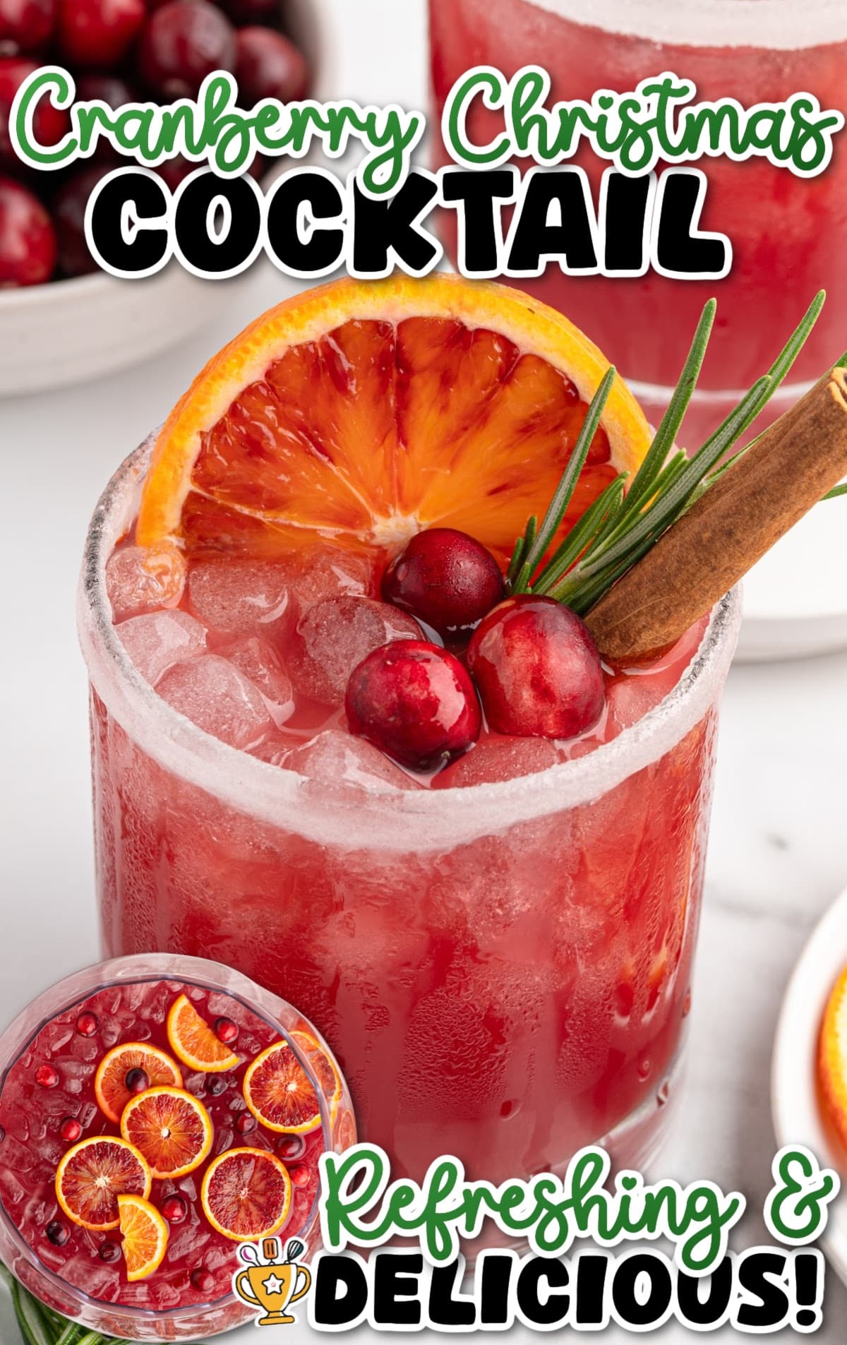 Cranberry Christmas cocktail in a short glass with crushed ice, topped with blood orange slices, fresh cranberries, rosemary sprig, and cinnamon stick on a white background.