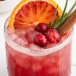 Cranberry Christmas cocktail in a rocks glass with crushed ice, blood orange slices, fresh cranberries, rosemary, and cinnamon stick, shown as a festive holiday cocktail pin image.