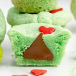 A green Grinch cookie with a red heart on top, split open to show a Hershey kiss in the middle.