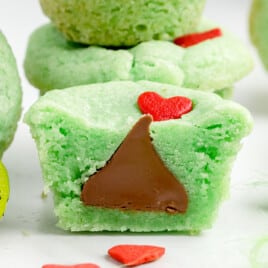 A green Grinch cookie with a red heart on top, split open to show a Hershey kiss in the middle.