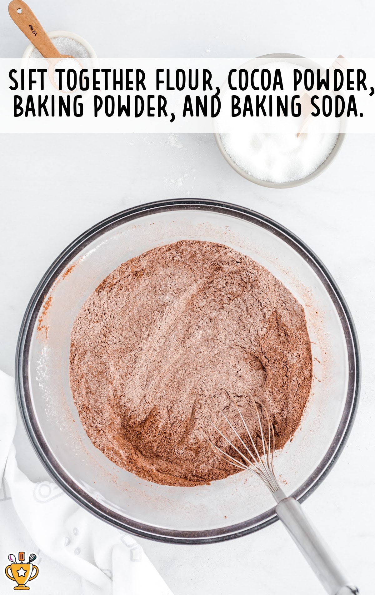 flour, cocoa powder, baking powder and baking soda mixed in a clear glass bowl with a whisker