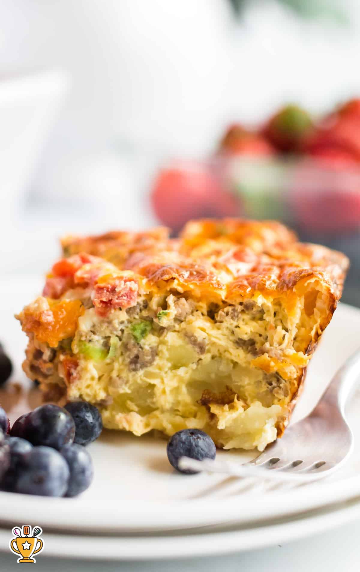 a piece of Sausage Breakfast Casserole on a white plate with a fork and some blueberries